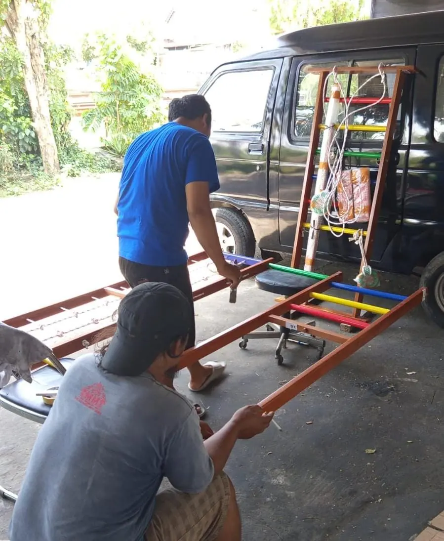 Pekerja menaikkan rangka permainan anak berwarna ke bak pikap