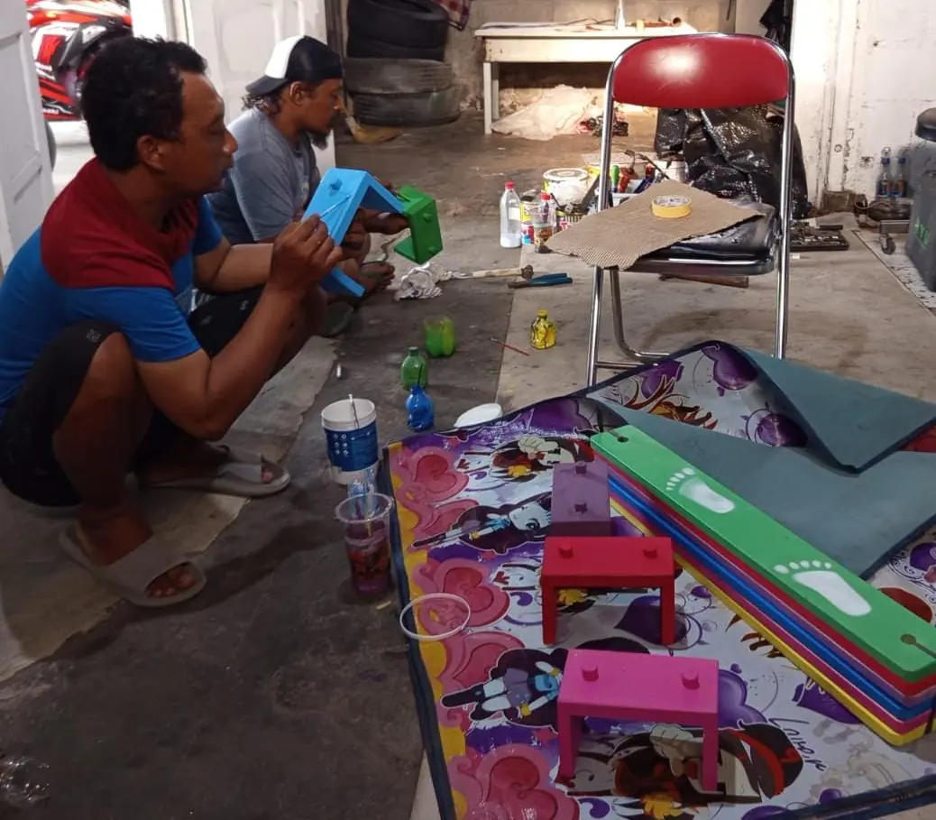 Dua pekerja merakit matras bermain bergambar dan perlengkapan permainan di dalam ruangan