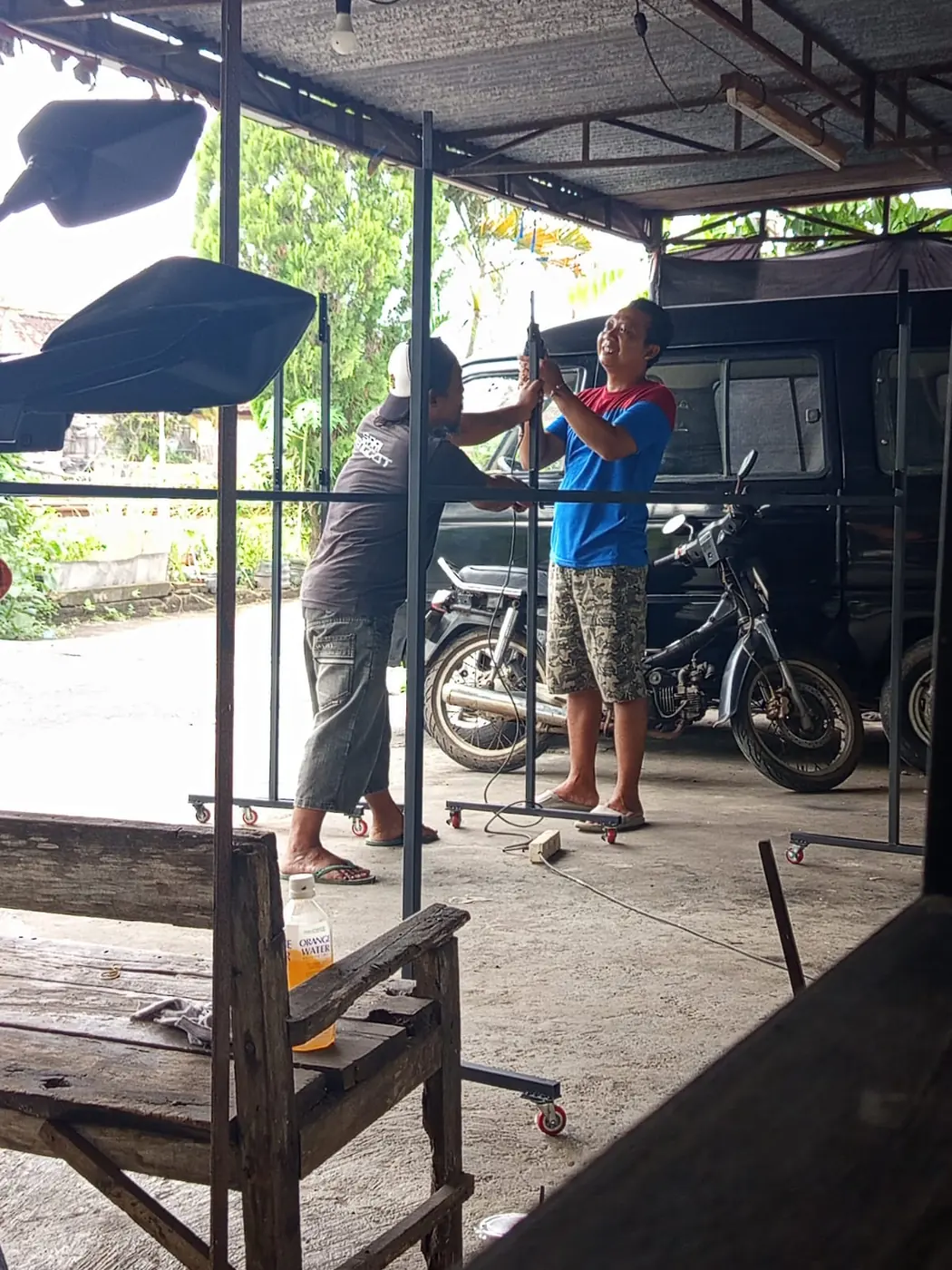 Dua pekerja mengelas rangka baja di halaman terbuka