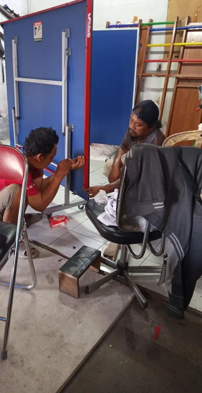 Dua pekerja merakit kaki dan dudukan kursi kantor