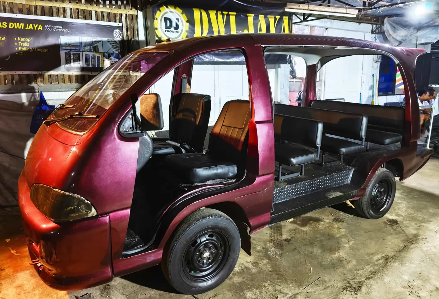 Kendaraan penumpang terbuka berwarna merah marun dengan tulisan Dwi Jaya