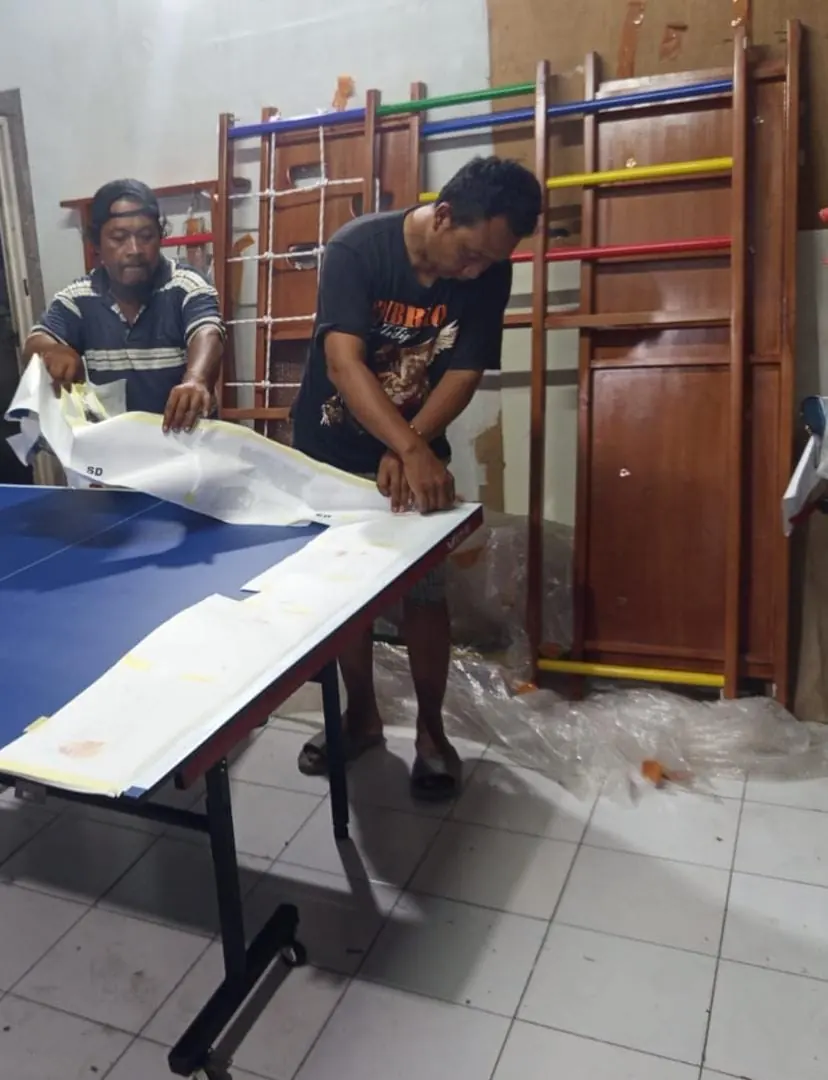Pekerja memasang lapisan permukaan biru pada daun meja pingpong