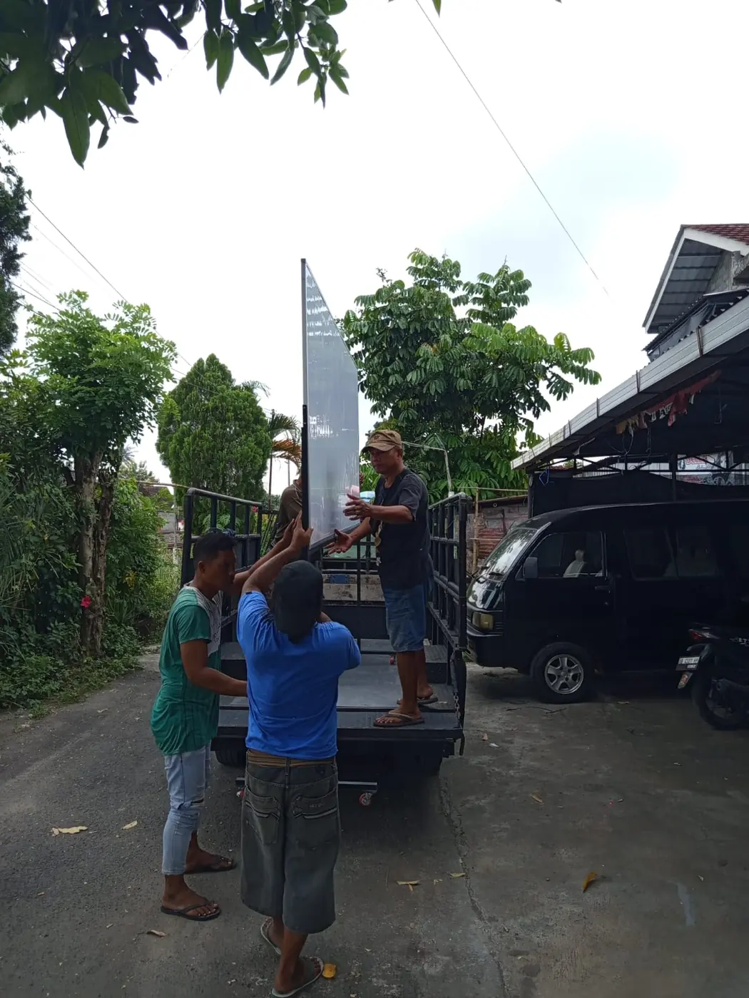 Dua pekerja menaikkan papan tulis ke bak mobil pikap untuk dikirim