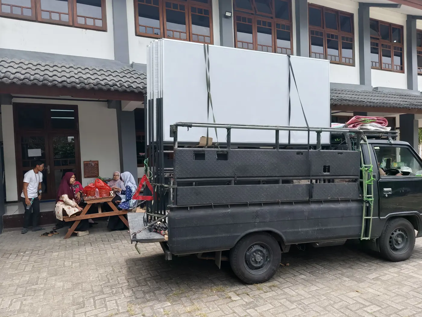 Rangka besi dan lembar papan putih dimuat di pikap di halaman sekolah
